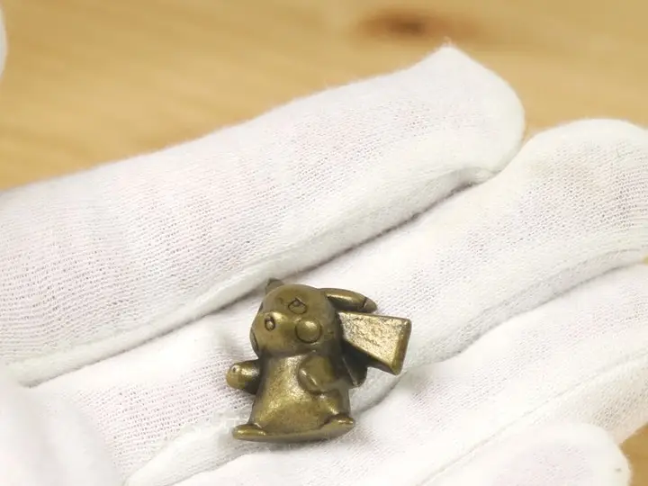 A small full-body bronze Pikachu figure held in a gloved hand